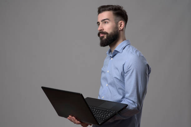 istock Confident handsome successful business man holding laptop computer and looking away at copyspace 908605328