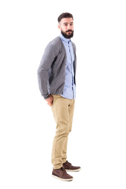 istock Young stylish bearded man in cardigan with hands in back pockets looking at camera. 908611266