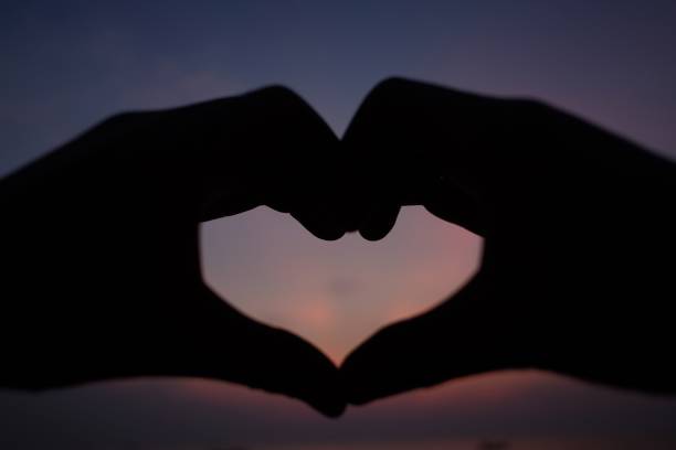 istock silhouette heart-shaped by hand sunset background 908622764
