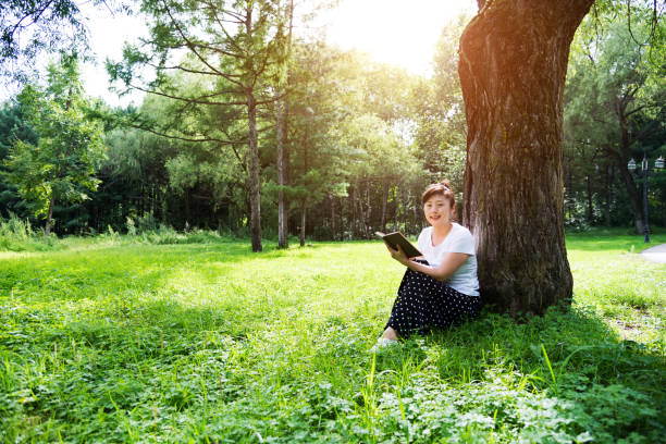 istock Woman reading a book under the tree 908626328