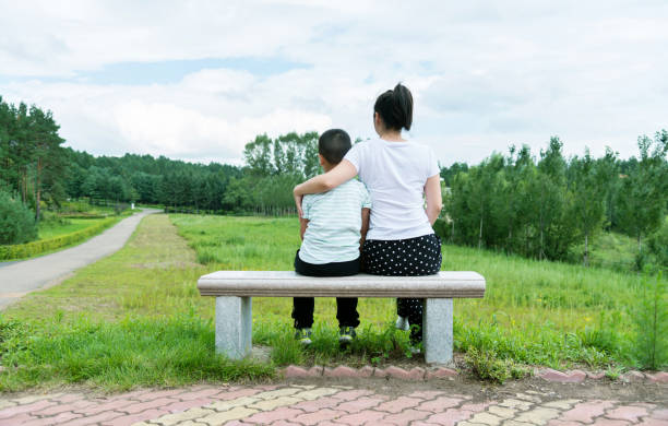 istock Mother and son sitting on park bench 908626732