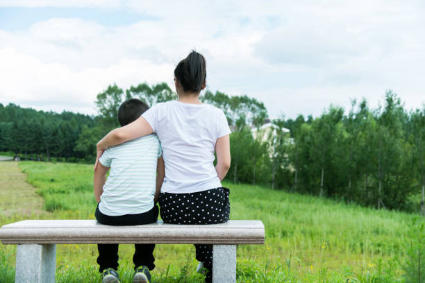 istock Mother and son sitting on park bench 908628536