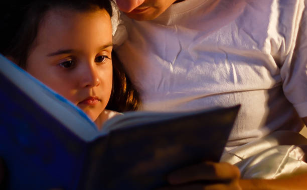 Caring father is reading a book to his little daughter before bedtime