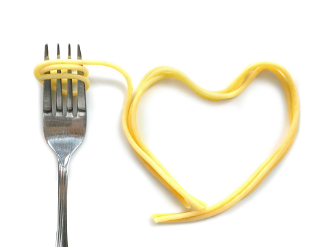 Heart shaped cooked capellini spaghetti with fork isolated on white background