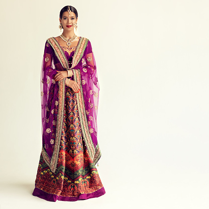 Young attractive woman, dressed in a traditional indian suit-sari. Splendid jewelry set, purple blouse and shawl (dupatta) with gilded hand-made decoration. Portrait in a full height.