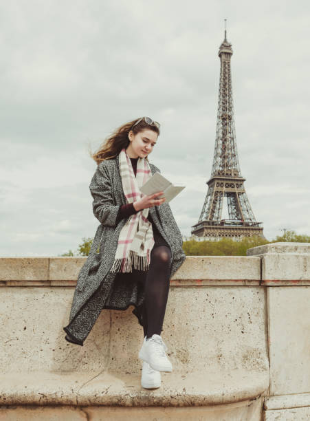 istock Young woman reading book on seine river coastline 908683262