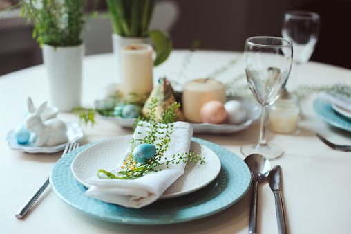 easter and spring festive table decorated in blue and white tones in natural rustic style, with eggs, bunny, fresh flowers and candles.