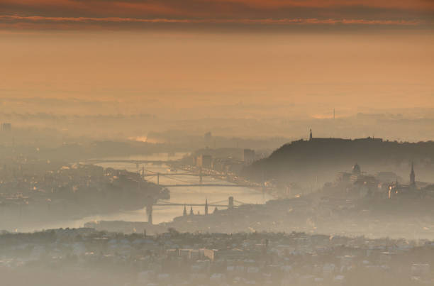 Downtown Budapest capital at sunrise in glowing winter morning mist and clouds with bridges over curving Danube river and Gellert Hill with Liberty Statue and Castle Hill at Buda side, Hungary Europe
