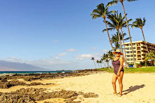 Senior Hispanic woman in bathing suit and sunhat on deserted Maui beach