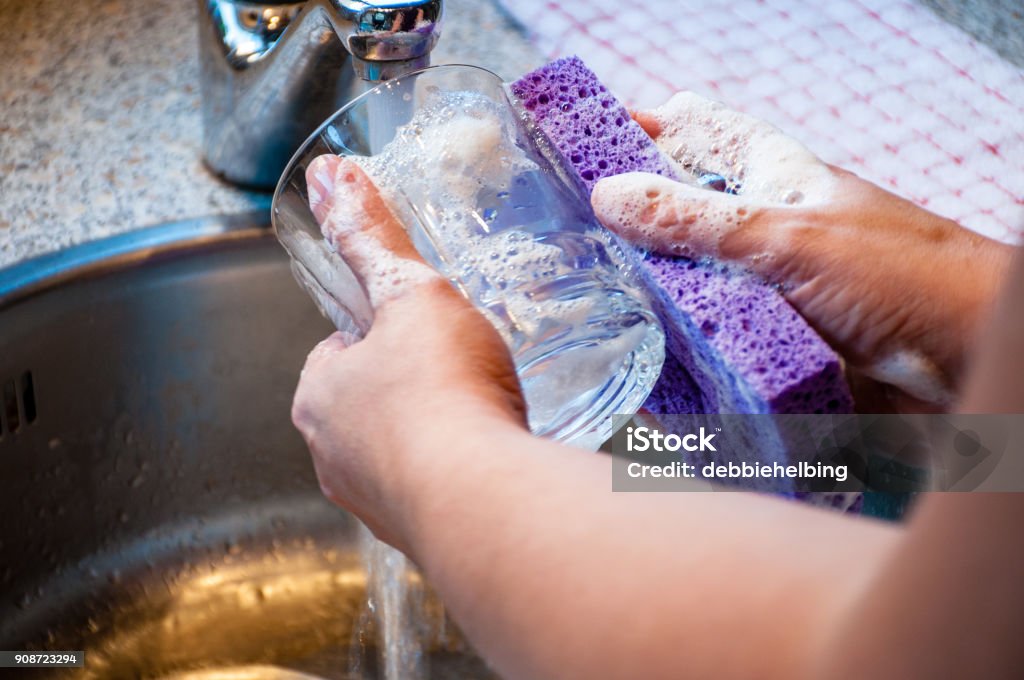 Woman Hand-Washing Dishes Woman hand-washing a drinking glass with soapy sponge in kitchen sink. Crockery Stock Photo