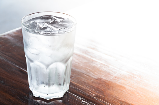 Female is holding glass of water full of ice cubes at the beach.