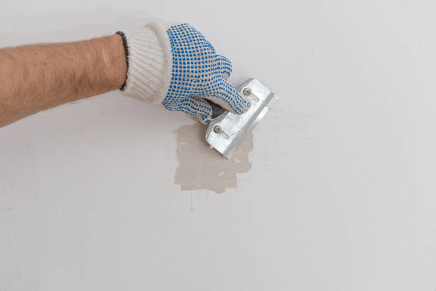 istock Worker removes old paint from concrete wall with scraper 908733938