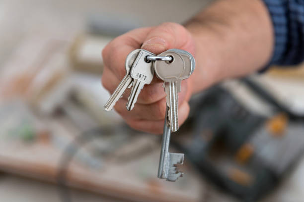 istock Man's hand holding keys with a construction in background 908734416