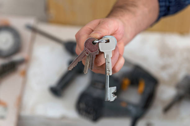 istock Man's hand holding keys with a construction in background 908734458
