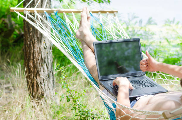 istock Young man in a hammock working on a laptop, concept of work on vacation, freelancing. 908737936