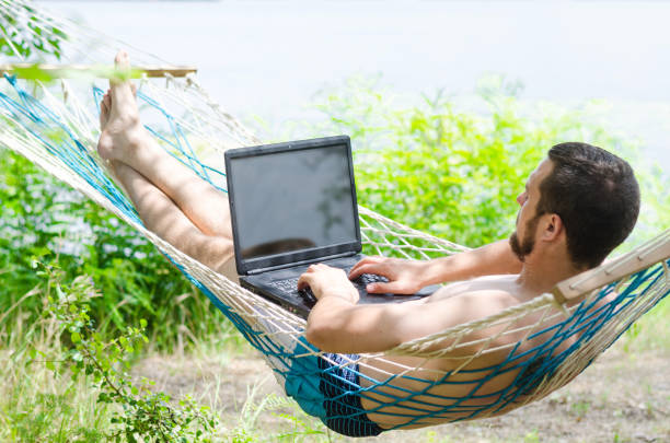 istock Young man in a hammock working on a laptop, concept of work on vacation, freelancing. 908737942