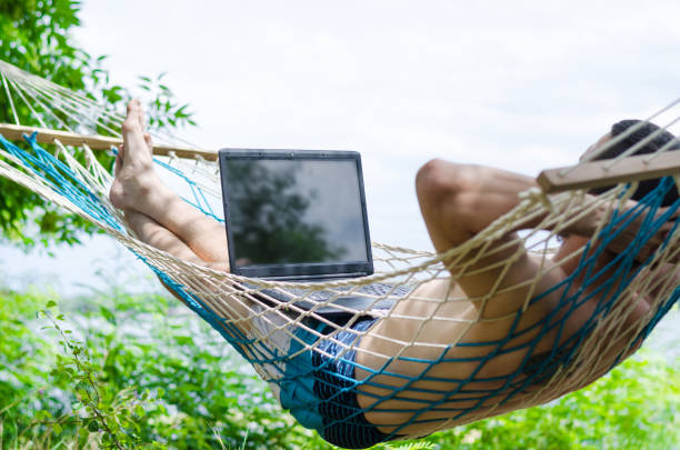 istock Young man in a hammock working on a laptop, concept of work on vacation, freelancing. 908737964