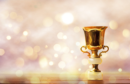 Golden trophy on wooden table, bokeh and glitter background with copy space
