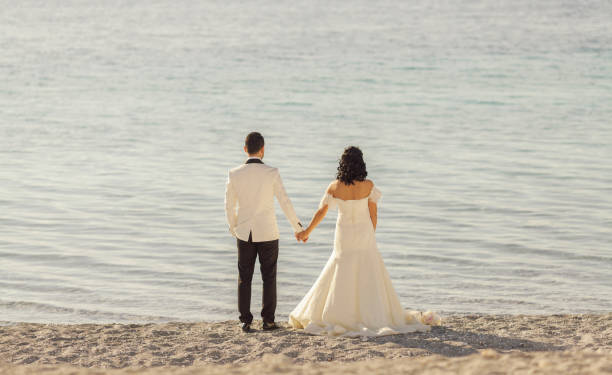 istock Bride and groom holding hands on the beach 908744978