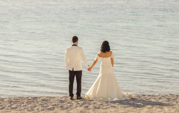 istock Bride and groom holding hands on the beach 908745076