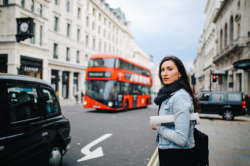 Young woman walking on the streets of central London, wearing a denim jacket and a scarf.