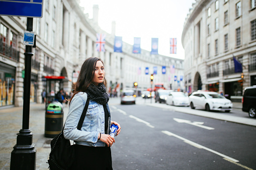Young woman walking on the streets of central London, wearing a denim jacket and a scarf.