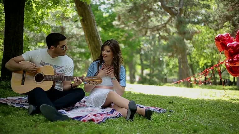 Man playing guitar to his girl on a picnic