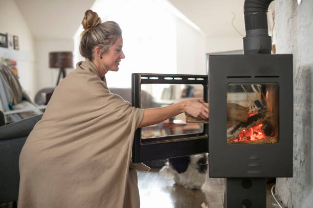 istock Beautiful middle-aged woman inserts wooden logs into the fireplace. 908763598