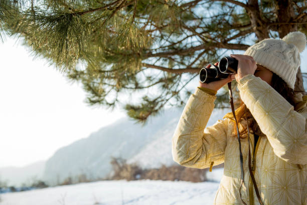 istock The girl in a White cap with a backpack in the winter in a forest looking through binoculars 908771266
