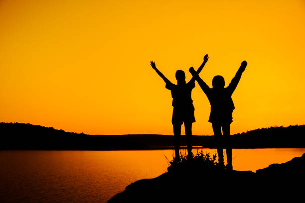 istock Silhouette People With Arms Raised Standing At Lakeshore Against Clear Sky During Sunset 908800244