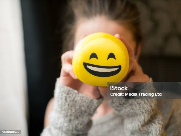 Girl Holding Smiley Face Laughing Emoticon In Front Of Her Face Stock Photo - Download Image Now