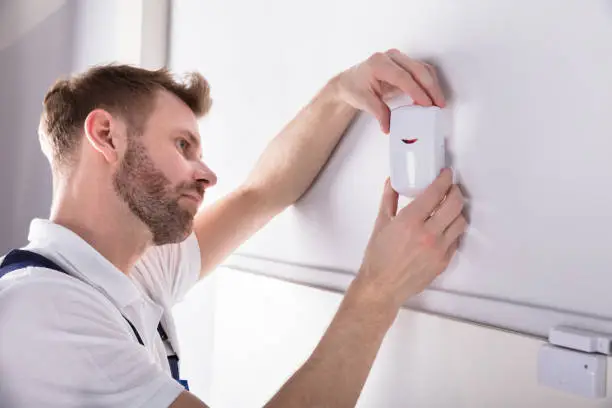 Close-up Of Young Male Electrician Installing Security System Door Sensor On Wall