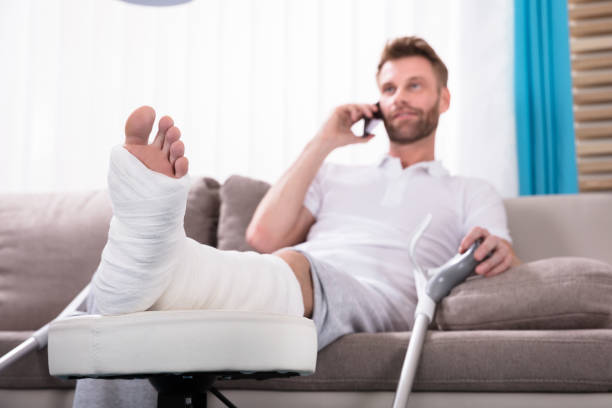 istock Happy Young Man With Broken Leg Talking On Smartphone 908801812