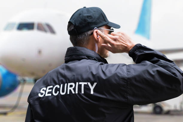 Security Guard Listening To Earpiece Against Building Rear view of mature security guard listening to earpiece against building security staff photos stock pictures, royalty-free photos & images