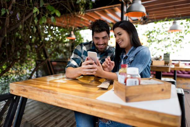 istock Couple looking at pictures on a cell phone at a restaurant 908849942