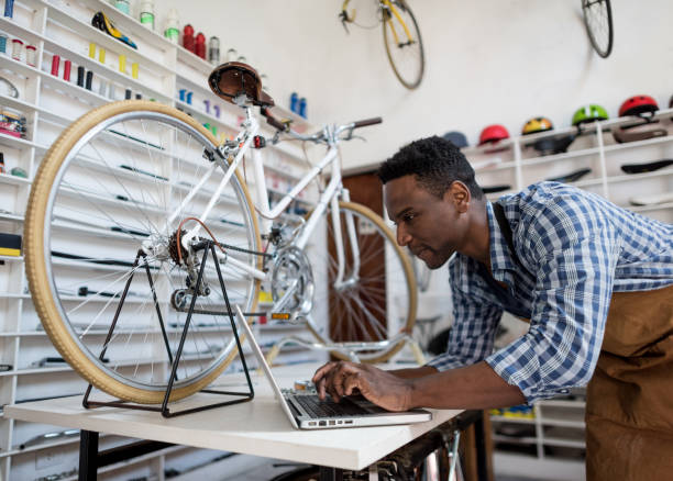 Black business owner of a bike shop checking the online orders on a laptop looking very happy Black business owner of a bike shop checking the online orders on a laptop looking very happy and smiling bicycle shop stock pictures, royalty-free photos & images