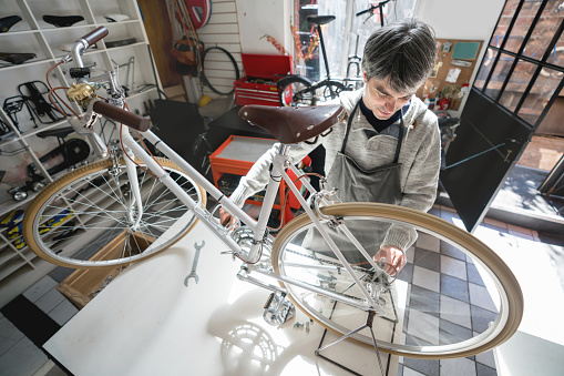 Manual worker at a bike shop adjusting the gear of a vintage bicycle on a table using  bike stand