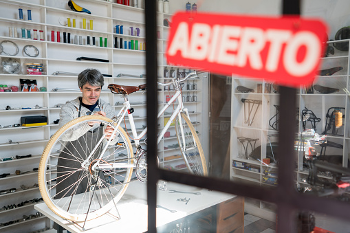 Open sign at a bicycle workshop and adult man fixing a vintage bike on a table at the background looking very focused