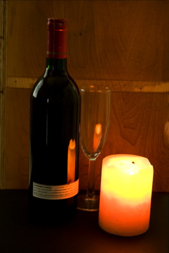 Burning candle is focus of this image with a wine bottle and glass by it's side.  Bottle and glass in soft focus.