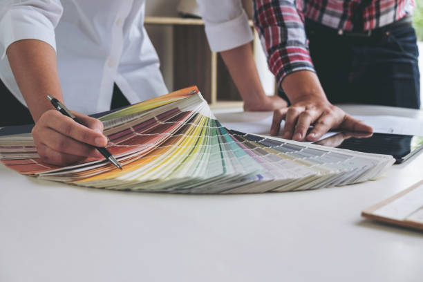 istock Two young women interior design or graphic designer working on project of architecture drawing with work tools and color swatches, colour chart in digital tablet at workplace 908871816