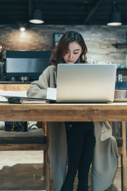 istock woman doing paperwork with laptop in coffee shop 908871960