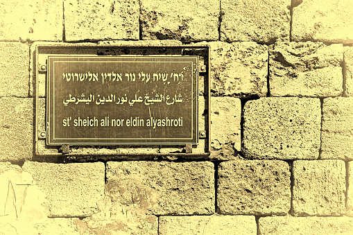 Pointer information in the Arab city of Akko.  Information street sign in Israel. Sheich Ali street road sign in front of a old stone wall in Israel city of Acre. Vintage style toned picture