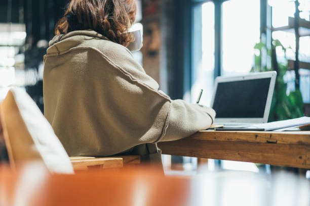 istock woman doing paperwork with laptop in coffee shop 908881810