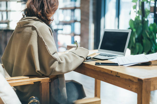 istock woman doing paperwork with laptop in coffee shop 908881946