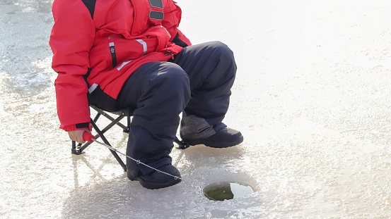 Trout ice fishing. A boy waiting with a fishing rod in an ice hole.