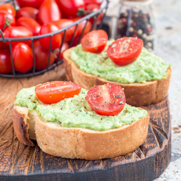 istock Open sandwiches with mashed avocado and cherry tomatoes on toasted bread, sprinkled with black pepper, square 908893782