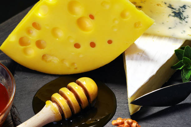 Close-up of varieties of cheeses with honey and nuts on a dark wooden table.