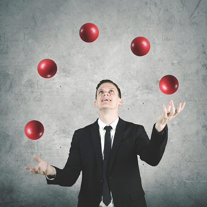 Picture of male entrepreneur wearing formal suit while juggling many red balls