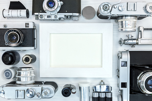 empty photo frame with old classic cameras, equipment and accessories on white wooden background flat view