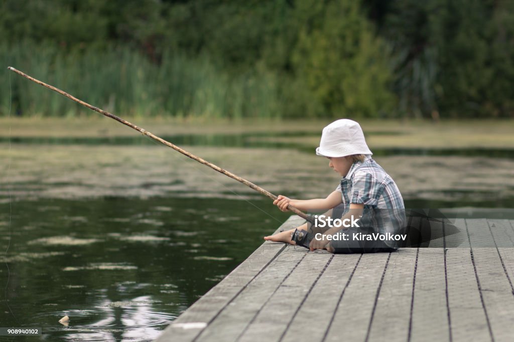 Niño con la tradicional caña de pescar en un muelle de madera - Foto de stock de Pescar libre de derechos